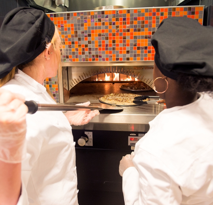 Students placing pizza in the pizza oven